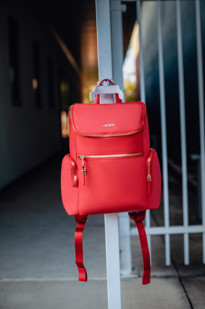 A red backpack hanging on the side of a pole.