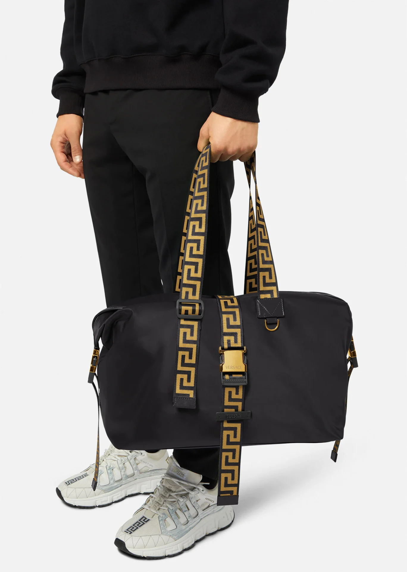 A person holding onto a black bag with gold straps