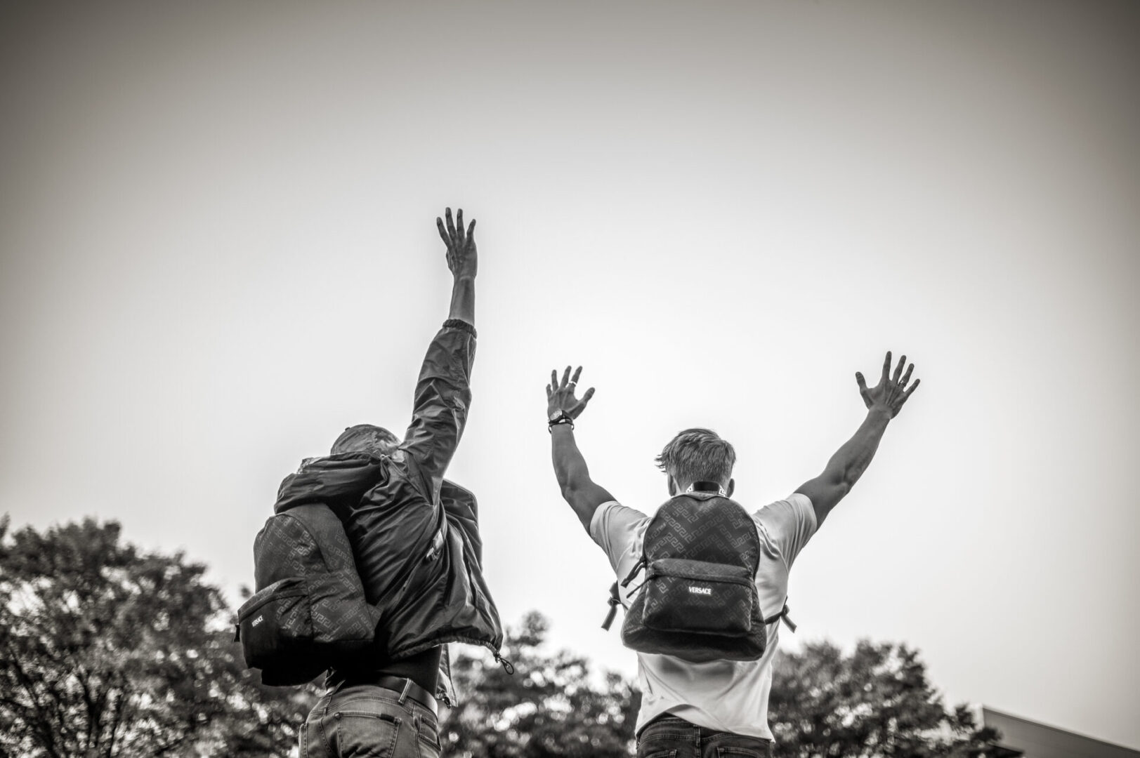 Two people with backpacks are reaching up for the sky.