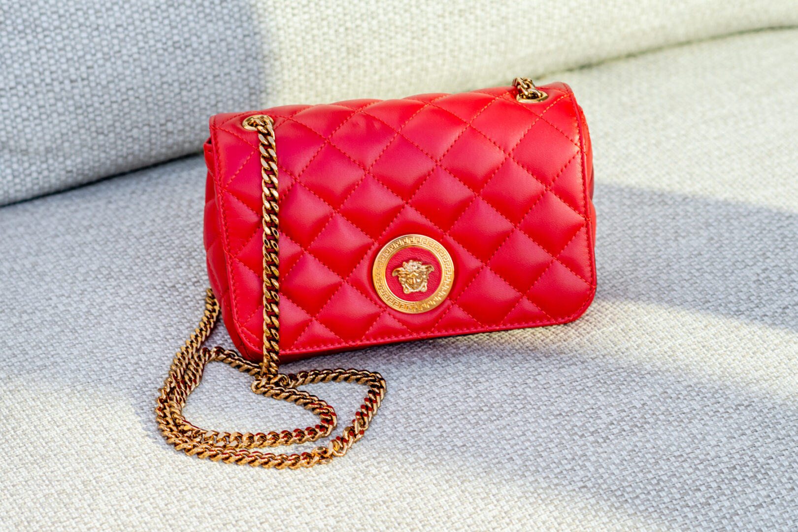 A red purse with gold chain on top of the couch.