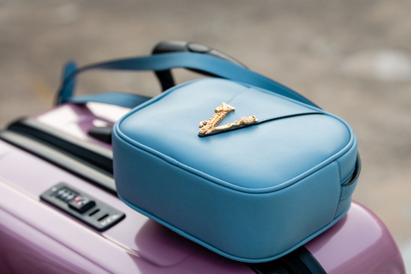 A blue purse sitting on top of a purple suitcase.