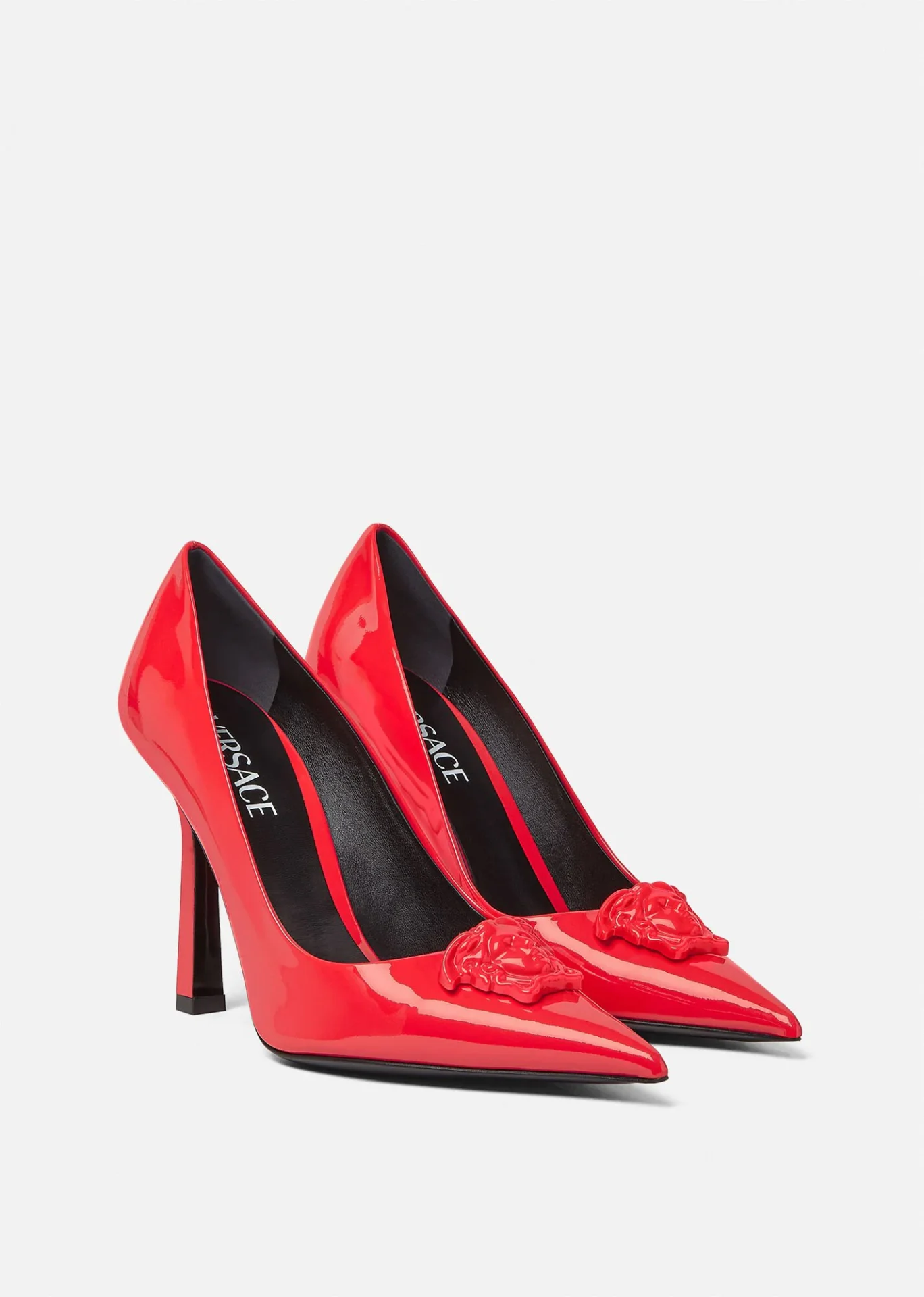 A pair of red high heels with a medusa head on the side.